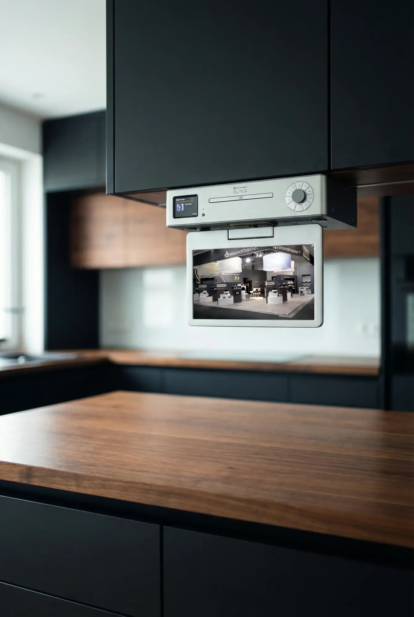 Silbergerahmtes digitales Display, das unter Küchenschränken montiert ist und einen Live-Feed von einer Ausstellung zeigt.